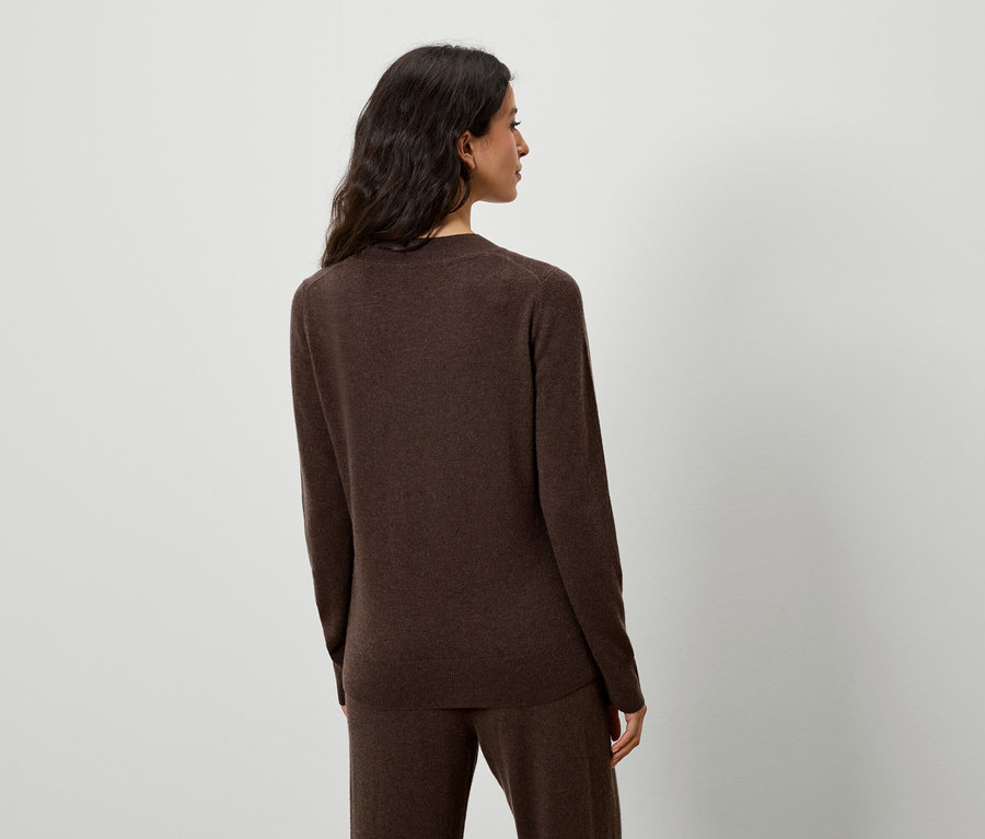 Frau posiert in braunem Pullover und Hose.