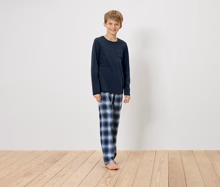 Junge steht auf Holzboden, trägt ein dunkelblaues, langärmliges Schlafanzugoberteil und eine blau karierte Schlafanzughose.