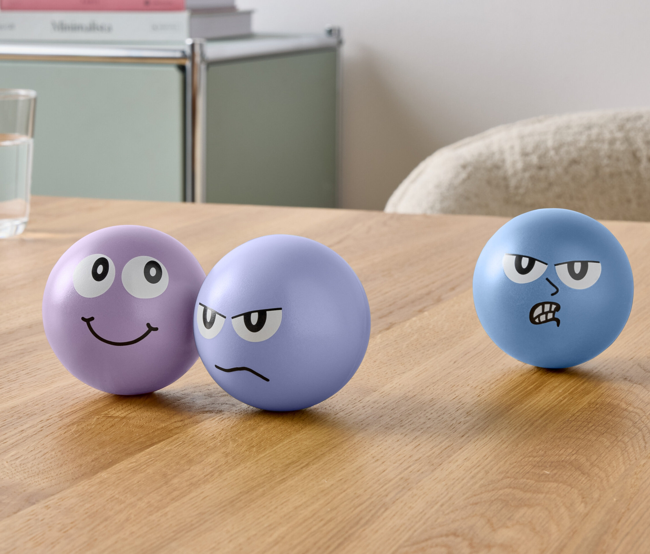 Drei Kugeln mit Gesichtern und ein Glas Wasser stehen auf einem Tisch.