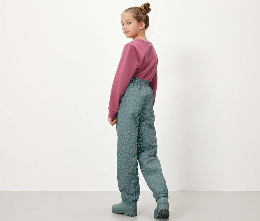 Mädchen mit Pullover und Kinder-Regenhose mit reflektierenden Elementen von hinten.