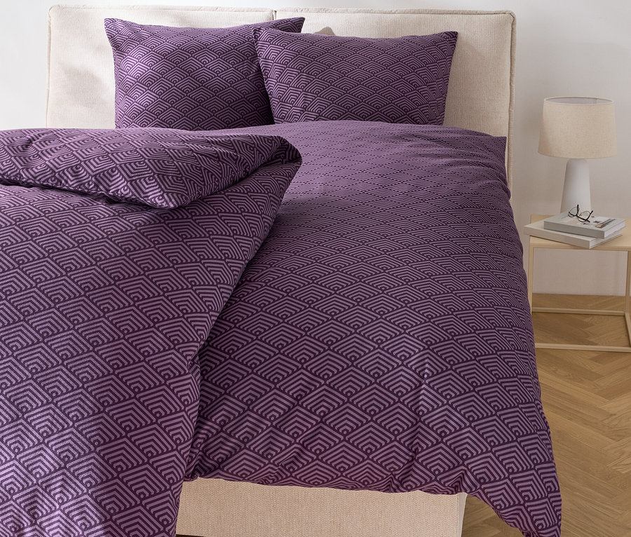 Bett mit lila geometrischer Bettwäsche und zwei Kissen.