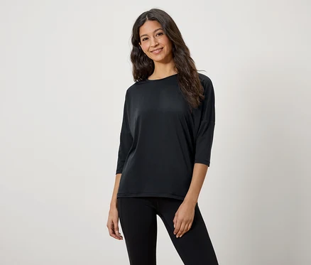 Eine Frau mit braunen Haaren posiert in einem schwarzen Dreiviertelarm-T-Shirt und schwarzen Leggings.