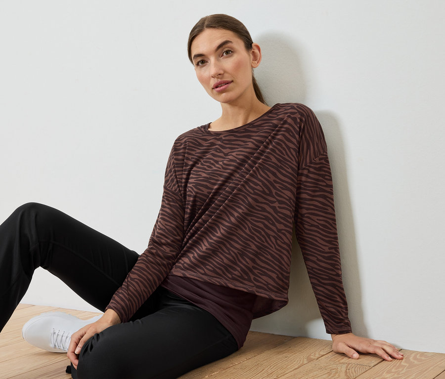 Frau sitzt auf dem Boden, trägt ein braun-schwarz gestreiftes Zebra-Top und schwarze Hosen.