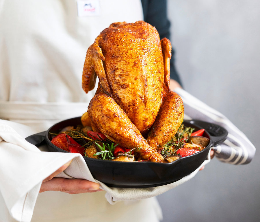 Person hält gebratenes Hähnchen im schwarzen STAUB Hähnchen-Bräter.