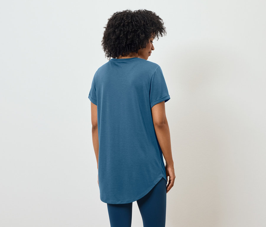Rückansicht einer Frau mit lockigem Haar in einem blauen T-Shirt und Leggings.