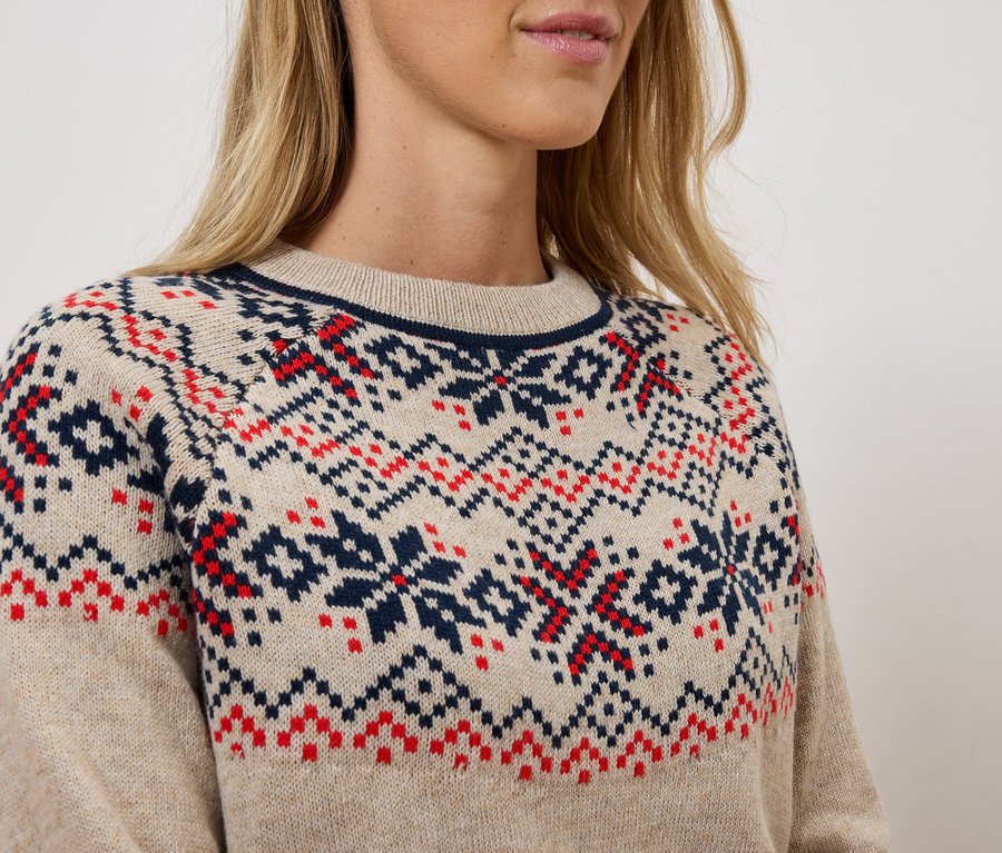 Detailaufnahme einer Dame, die einen beigen Strickpullover mit geometrischen roten und blauen Mustern trägt.