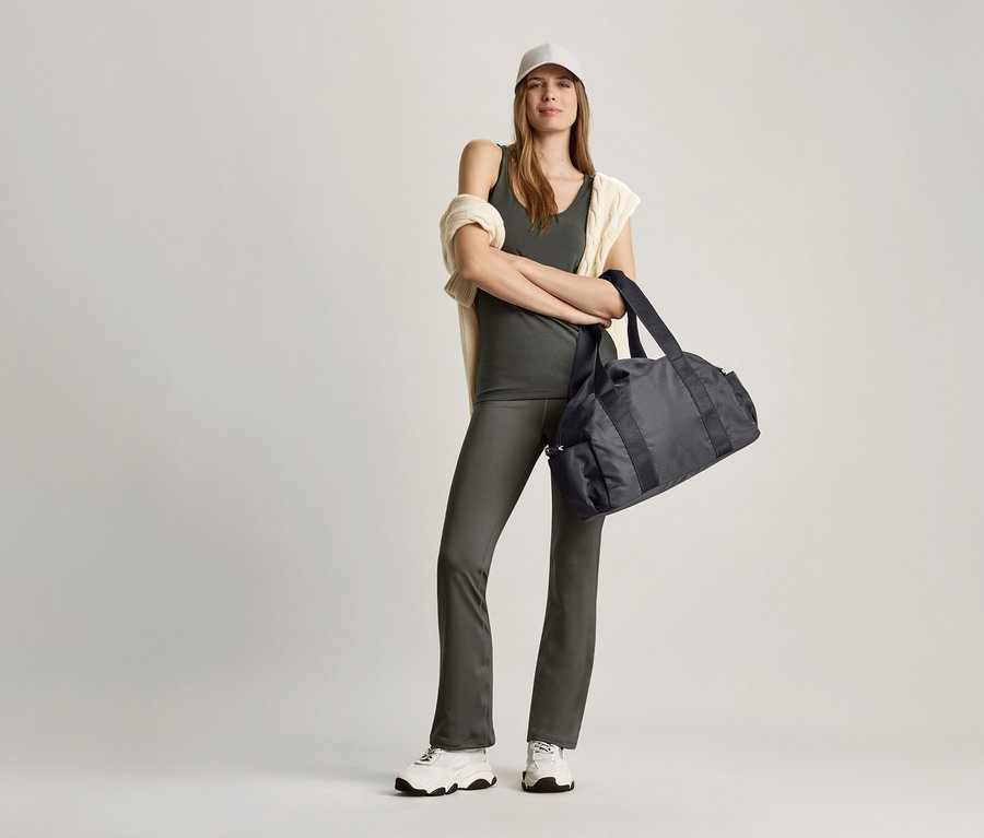 Frau posiert mit olivgrünem Top und schwarzer Sporttasche.