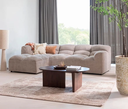 Wohnzimmer mit beigem Modulsofa, dunklem Couchtisch, gemustertem Teppich und Stehlampe.
