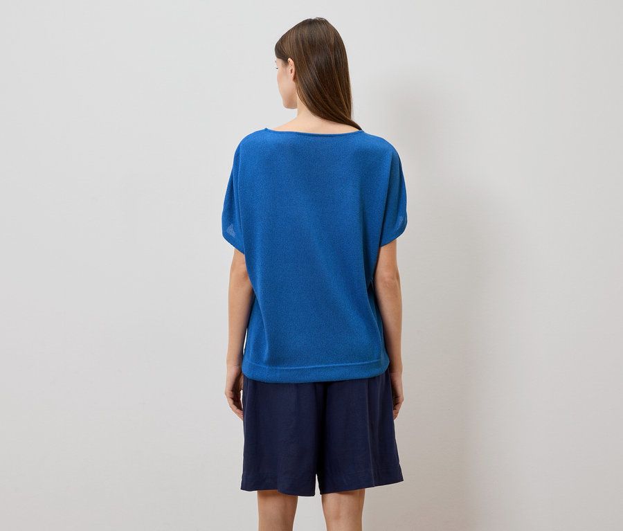 Rückansicht einer Frau mit langen braunen Haaren, die ein blaues T-Shirt und dunkelblaue Shorts vor einem weißen Hintergrund trägt.