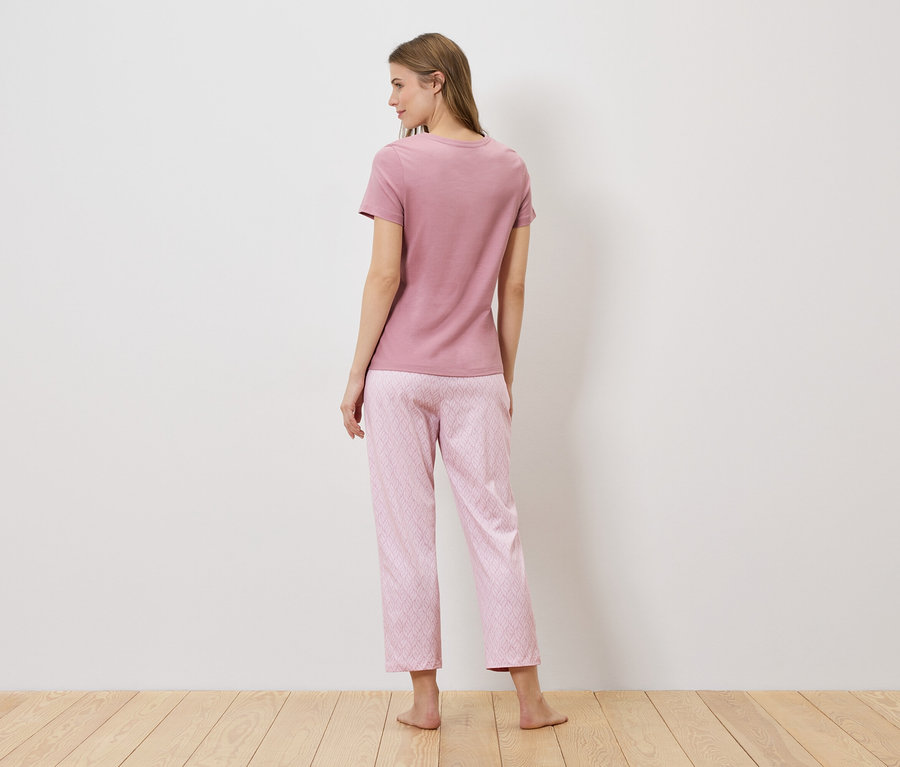 Rückansicht einer Frau mit langen Haaren, die ein rosafarbenes T-Shirt und eine rosafarbene Pyjamahose mit geometrischem Muster trägt.