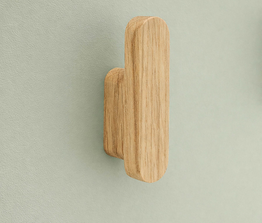 Nahaufnahme eines einzelnen, hellbraunen Holzmantelhakens an einer hellblaugrünen Wand.