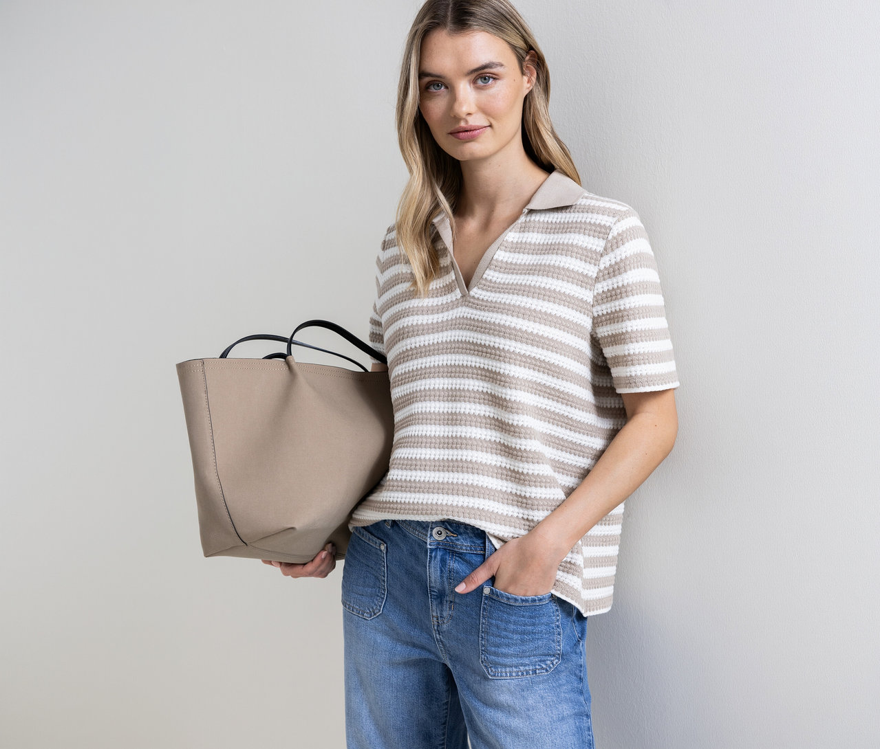 Frau mit beiger Tasche und gestreiftem Street One Strickshirt. Sie hat eine Hand in der Hosentasche.