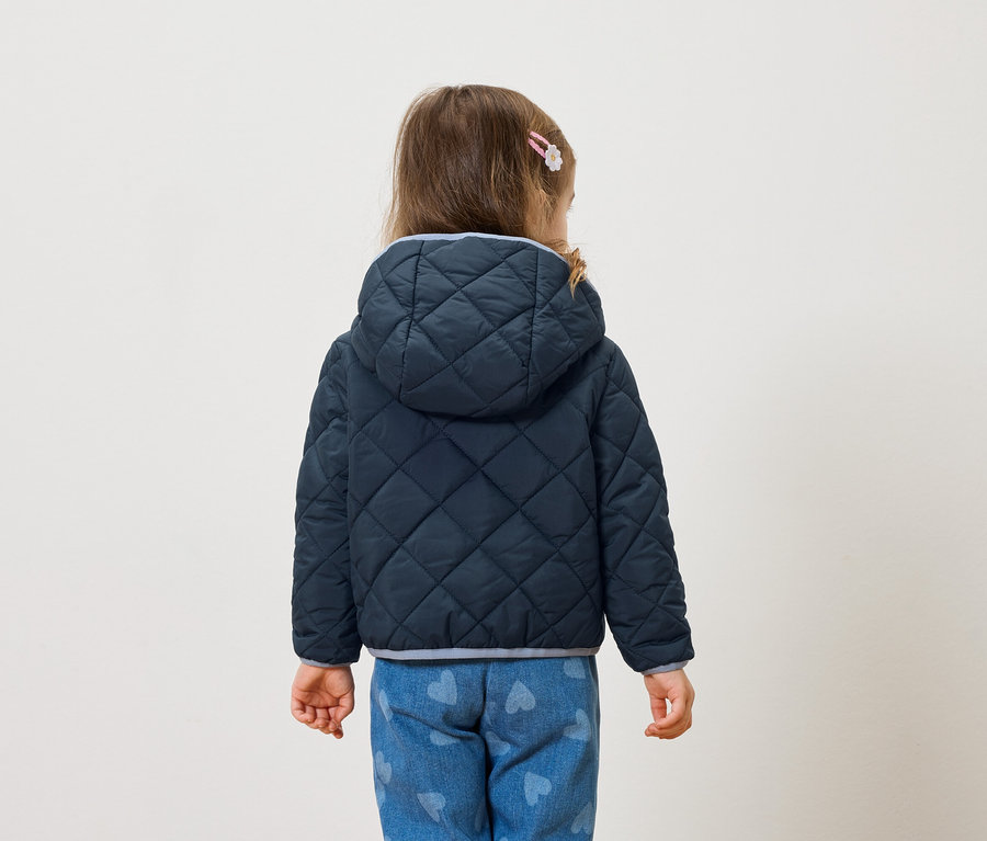 Rückansicht eines kleinen Mädchens mit Haarspange, das eine dunkelblaue gesteppte Jacke mit Kapuze und herzförmige Jeans trägt.