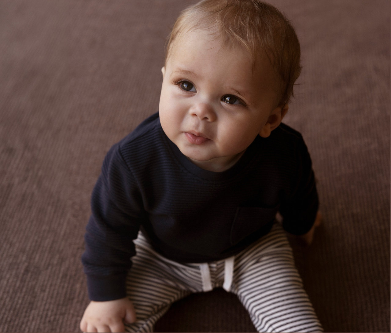 Baby sitzt auf dem Boden und trägt eine NAME IT Baby-Jerseyhose mit Streifen.