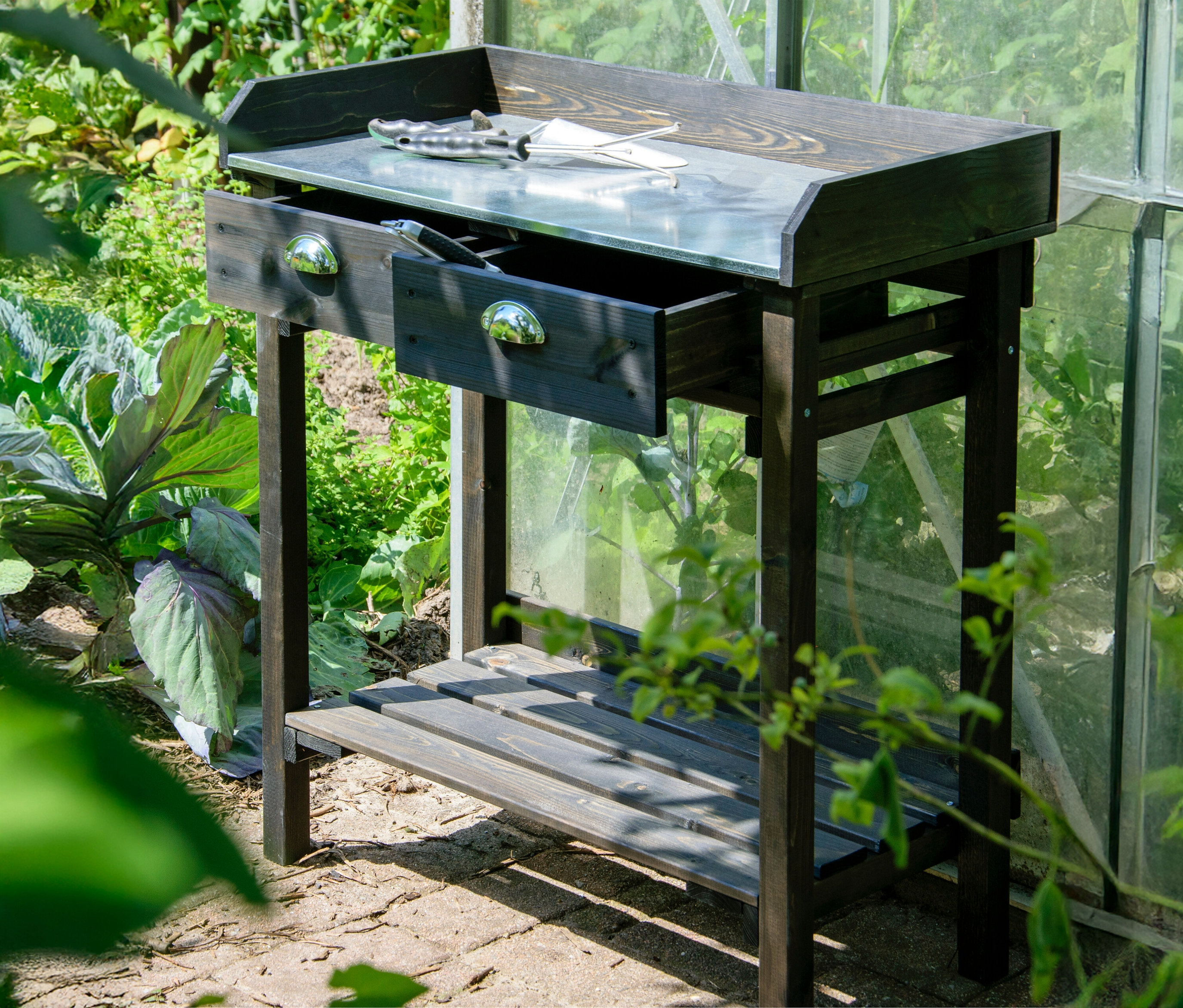 Ein schwarzer Pflanztisch mit Schubladen steht im Garten.