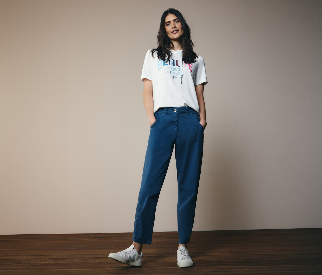 Frau mit CECIL Hoodie-Shirt und blauer CECIL Barrel »Scarlett« Hose steht mit Händen in den Taschen vor der Kamera.