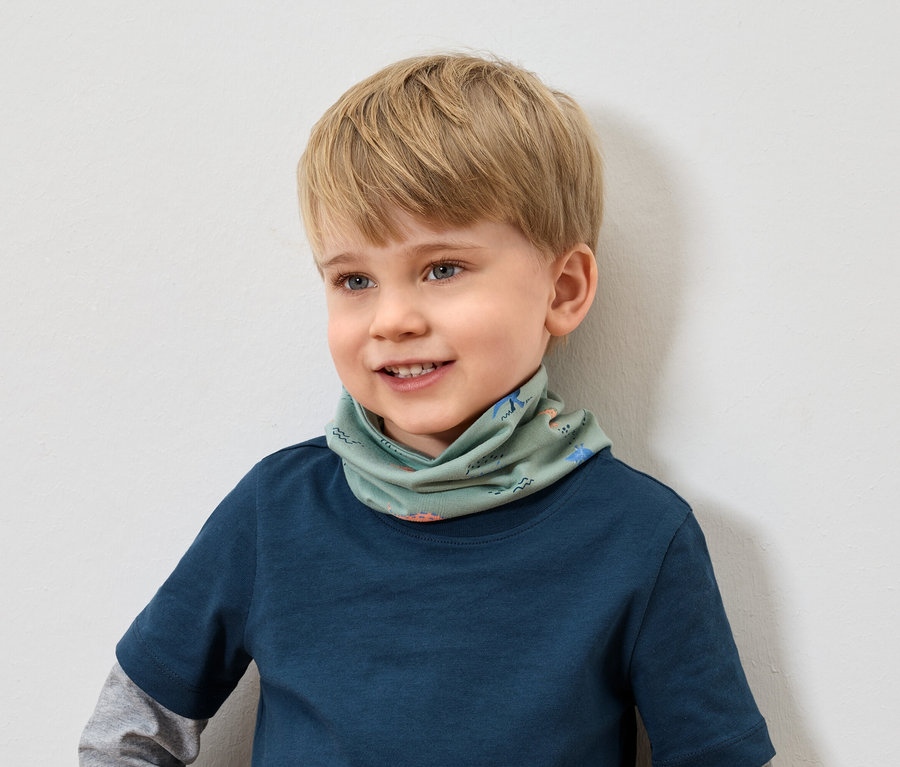 Lächelnder Junge mit blonden Haaren und blauem T-Shirt trägt einen grünen Schal mit Tiermuster.