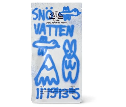Weisse Kaffeepackung mit blauem, sprühlackiertem Text und Grafiken. Oben steht "SNÖ VATTEN", darunter "Lykke Peru Agua de Nieve" und ein Regenbogen-Logo. Weitere blaue Sprühgrafiken zeigen einen Vogel, einen Berg und einen Hasen. Kleinerer Text beschreibt den Kaffee.
