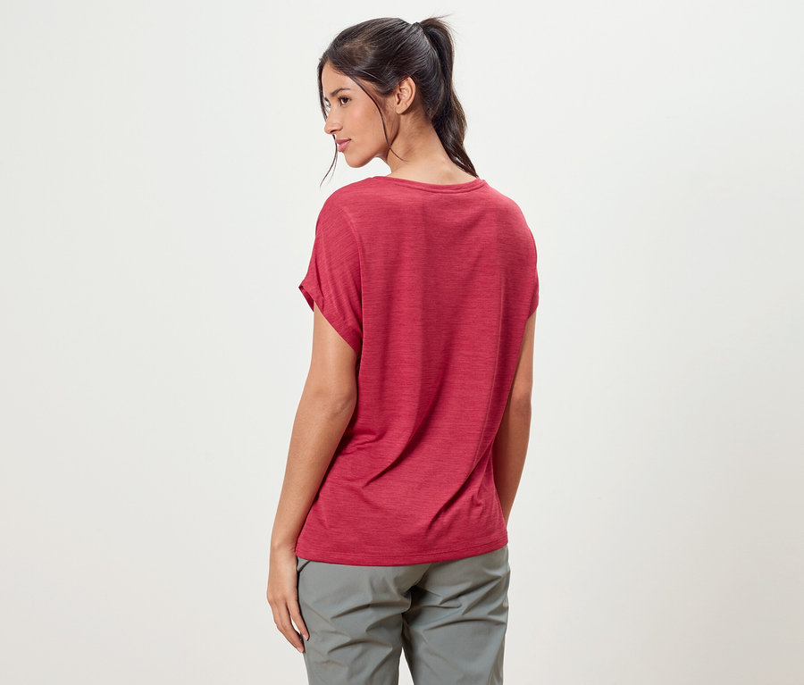 Eine Frau mit einem Pferdeschwanz trägt ein rotes T-Shirt und graue Hosen.