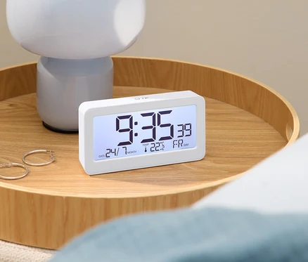 Digitaler Wecker mit Uhrzeit 9:35 auf einem Holztisch mit Lampe und Ohrringen.