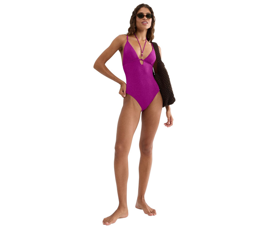 Frau mit Sonnenbrille, die einen violetten Badeanzug und eine braune Tasche trägt.