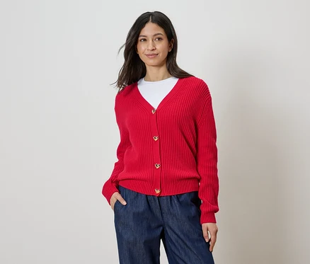 Frau trägt eine rote Strickjacke mit Herzknöpfen, ein weißes T-Shirt und blaue Hosen.