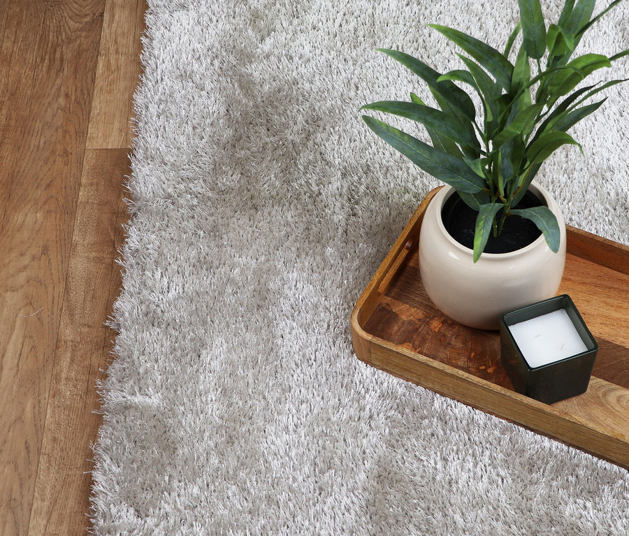 Nahaufnahme vom »Silky« Teppich in Creme mit Pflanze und Kerze auf einem Holztablett.