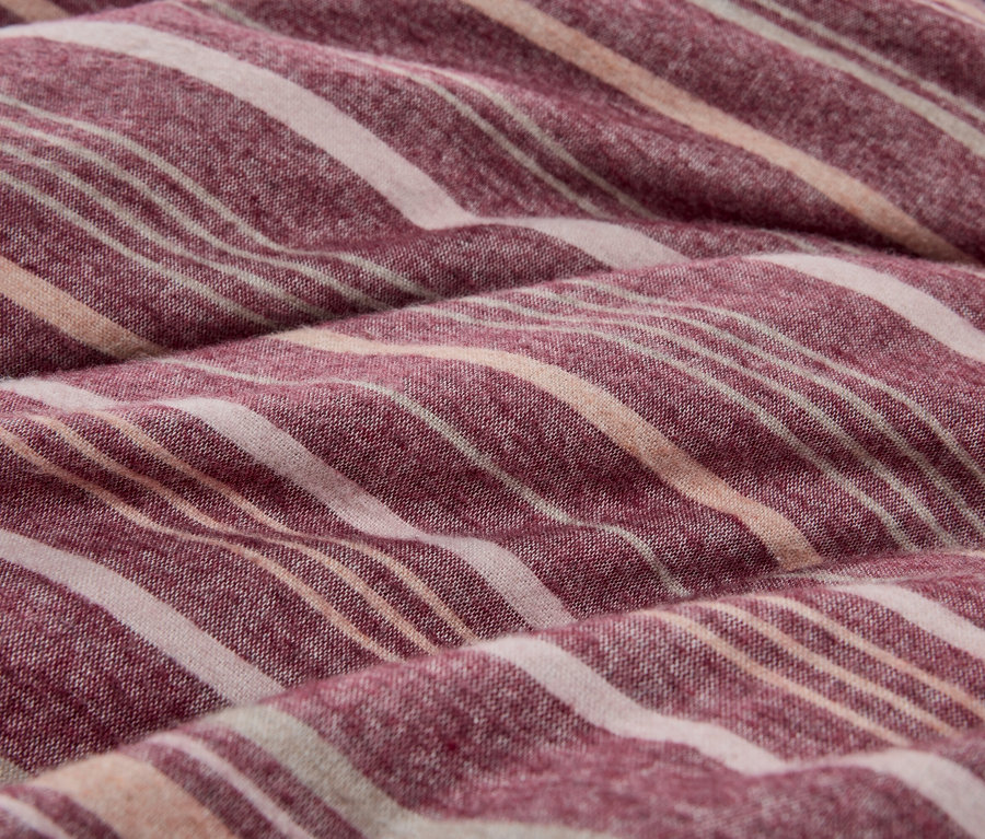 Nahaufnahme eines weichen, gefalteten Stoffes mit Streifen in Rot-Violett, Cremeweiß und hellem Pfirsich.