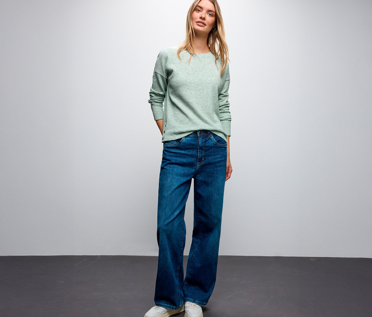 Blonde Frau trägt ein Street One Shirt mit Struktur, blaue Jeans und weiße Sneaker.