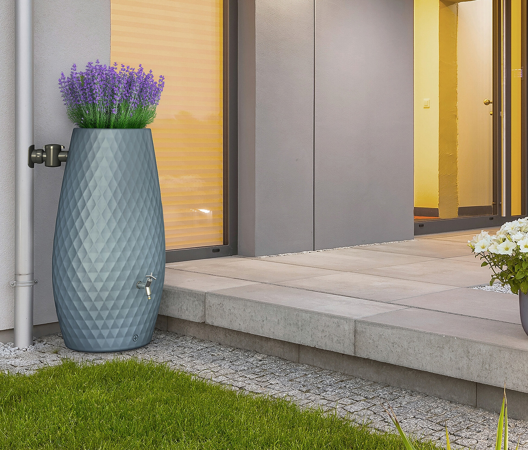 Eine blaue Regentonne mit Diamantenmuster steht neben einer Hauswand, bepflanzt mit lila Lavendel.