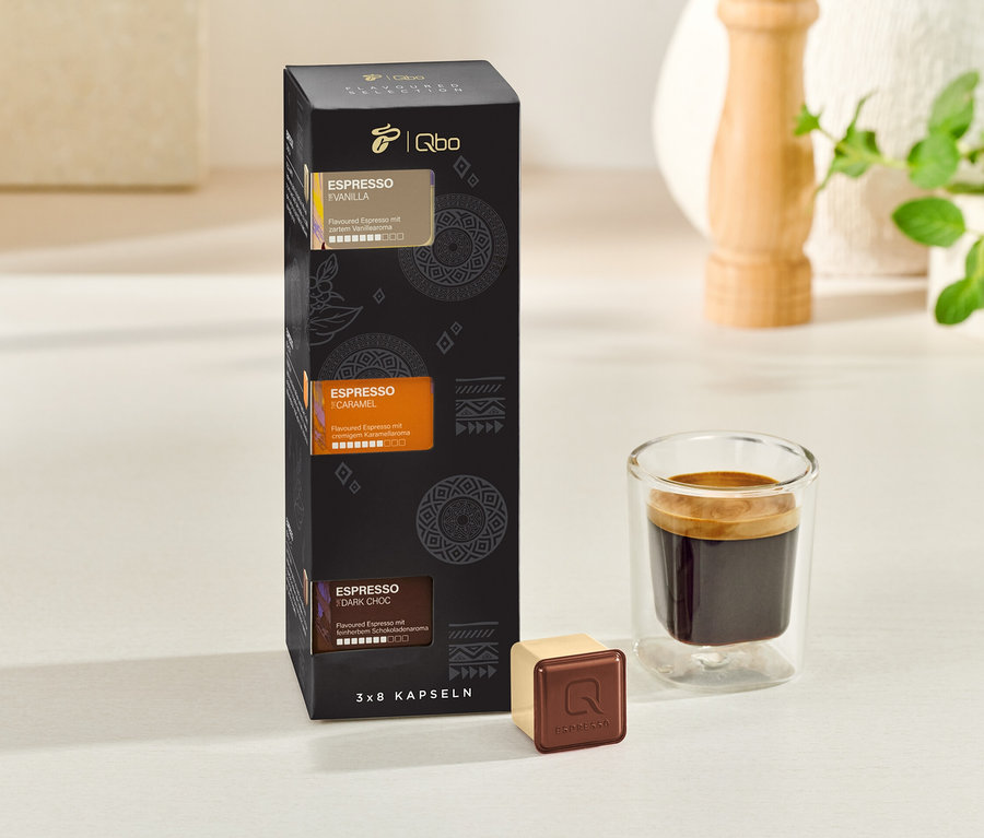Eine schwarze Schachtel Qbo Espresso Kapseln neben einer Tasse Espresso.