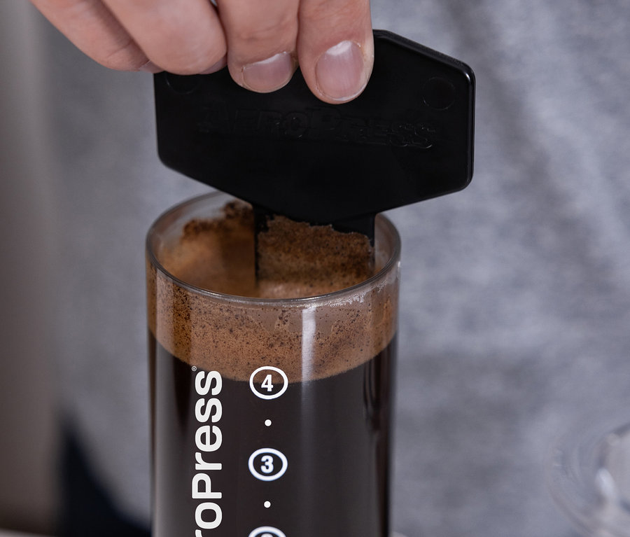 Hand drückt den Stempel des transparenten AeroPress Coffee Maker »Clear« in den Zylinder mit Kaffee.