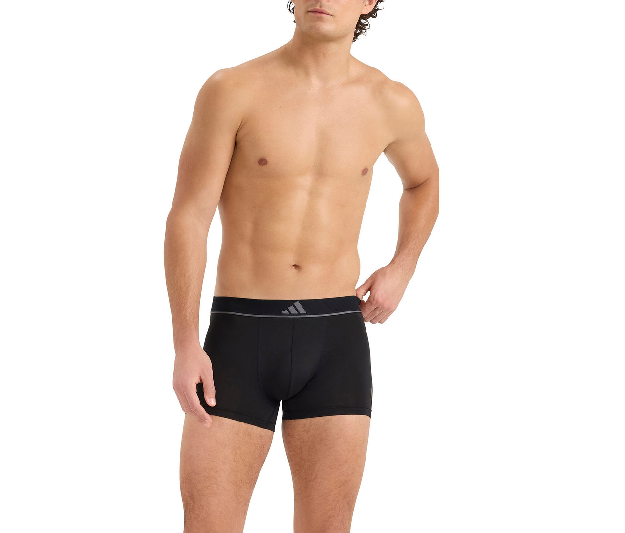 Oben ohne Mann in schwarzen Boxershorts mit grauem Bund und dreistreifigem Logo. Seine rechte Hand liegt am Bund.