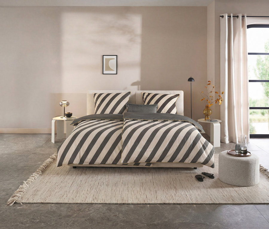 Dunkelgrau-beige gestreifte SCHÖNER WOHNEN-Kollektion Renforcé-Bettwäsche auf einem Bett in einem modernen Schlafzimmer mit hellem Teppich und Fenster.