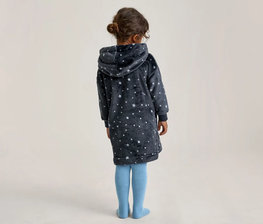 Kind von hinten gesehen, trägt ein dunkelblaues Kapuzenkleid mit weißen Sternen und hellblauen Strumpfhosen.