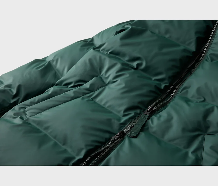 Nahaufnahme einer dunkelgrünen, gesteppten Daunenjacke mit schräg verlaufendem, teilweise geöffnetem schwarzem Reißverschluss.