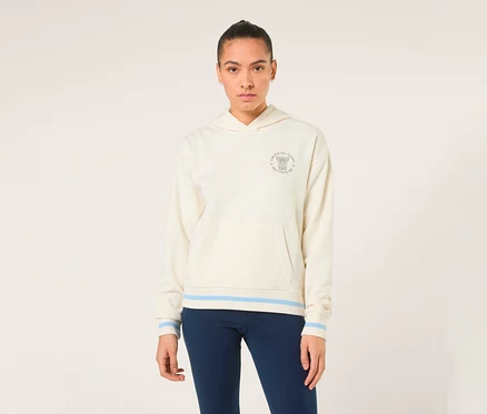 Eine Frau trägt einen off-white FILA Damen-Hoodie „MARLIA“ mit blauen Streifen an Saum und Ärmelbündchen sowie einem Logo auf der Brust.