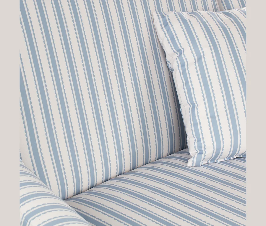 Nahaufnahme eines Sofas mit blau-weiß gestreiftem Stoffbezug und passendem Kissen. Die blauen Streifen haben gewellte Ränder.