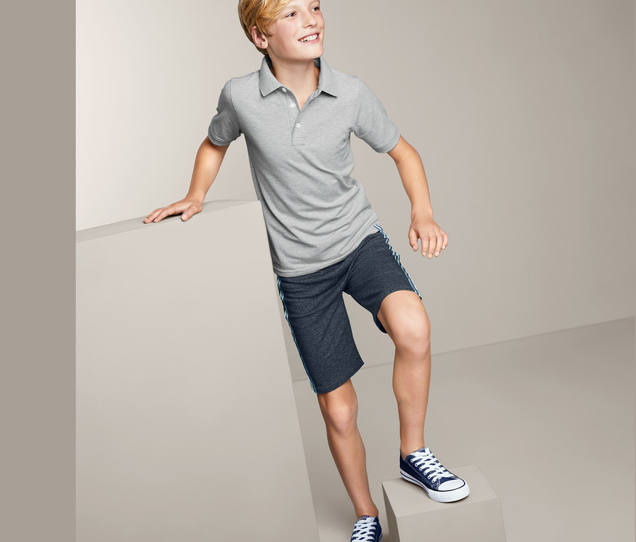 Ein Junge in einem grauen 2 Poloshirts und Shorts steht auf einem Würfel.