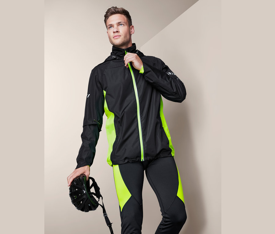 Mann schliesst eine schwarze Velo-Regenjacke mit neongrünen Details und hält einen Velohelm.