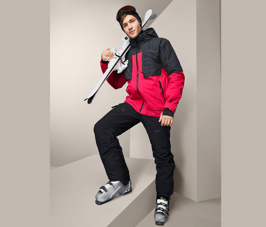 Mann mit Skiern auf der Schulter trägt eine High-End-Skijacke.