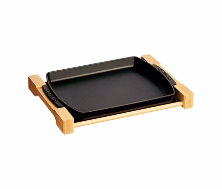 Schwarze rechteckige STAUB Servierpfanne auf einer Holzunterlage.