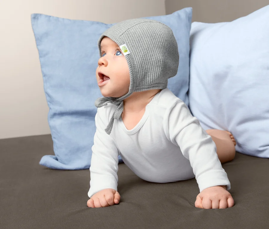 Baby liegt auf dem Bauch und trägt eine Babymütze.