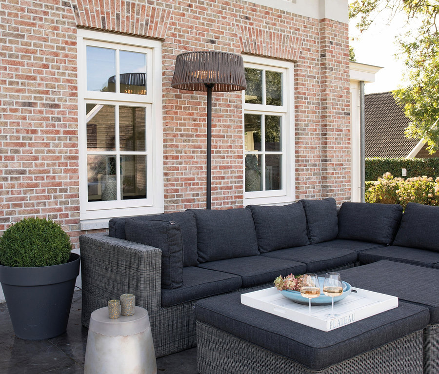 Eine Eckcouch mit Kissen und zwei Weingläser auf einem Tisch. Im Hintergrund steht ein Sunred-Stand-Heizstrahler »Artix Corda«.