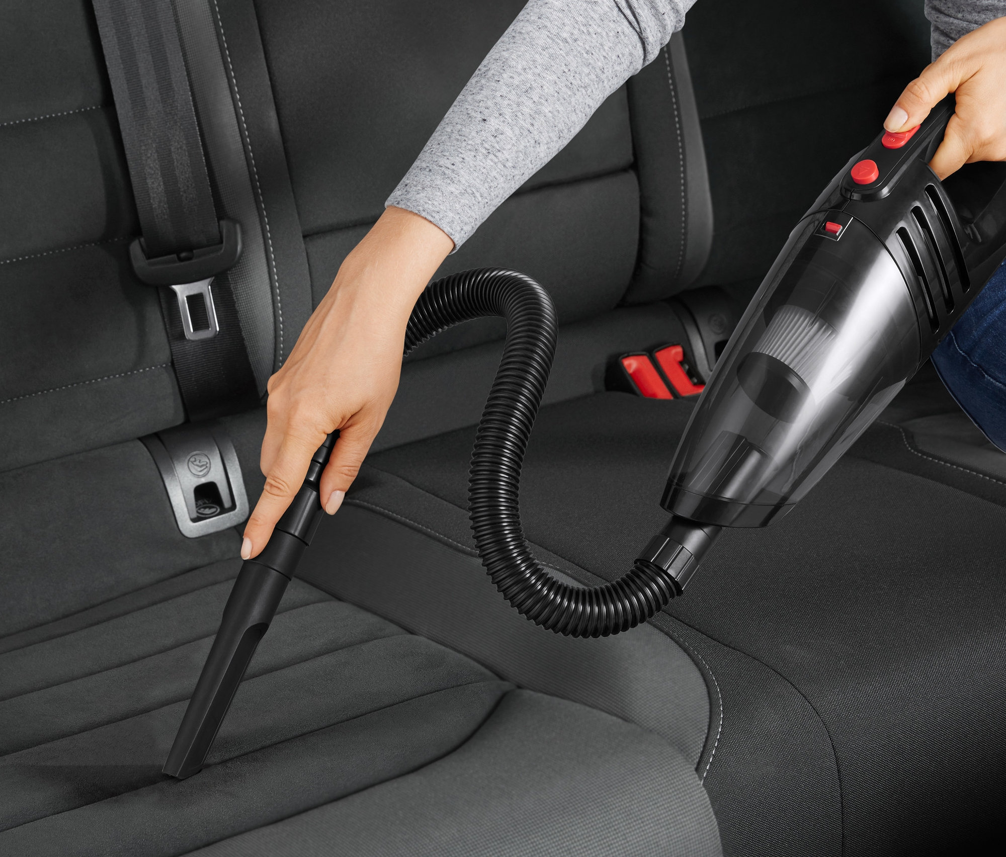 Frau saugt den Autositz mit einem Autostaubsauger.