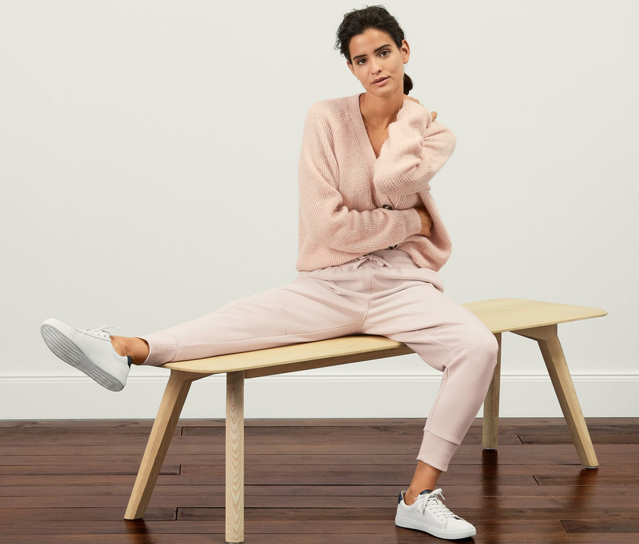Frau sitzt in Sweatpants und Pullover auf einer Bank.