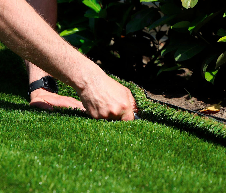 Mann verlegt Primaflor Kunstrasen »ARIZONA« entlang eines Gartenrands.
