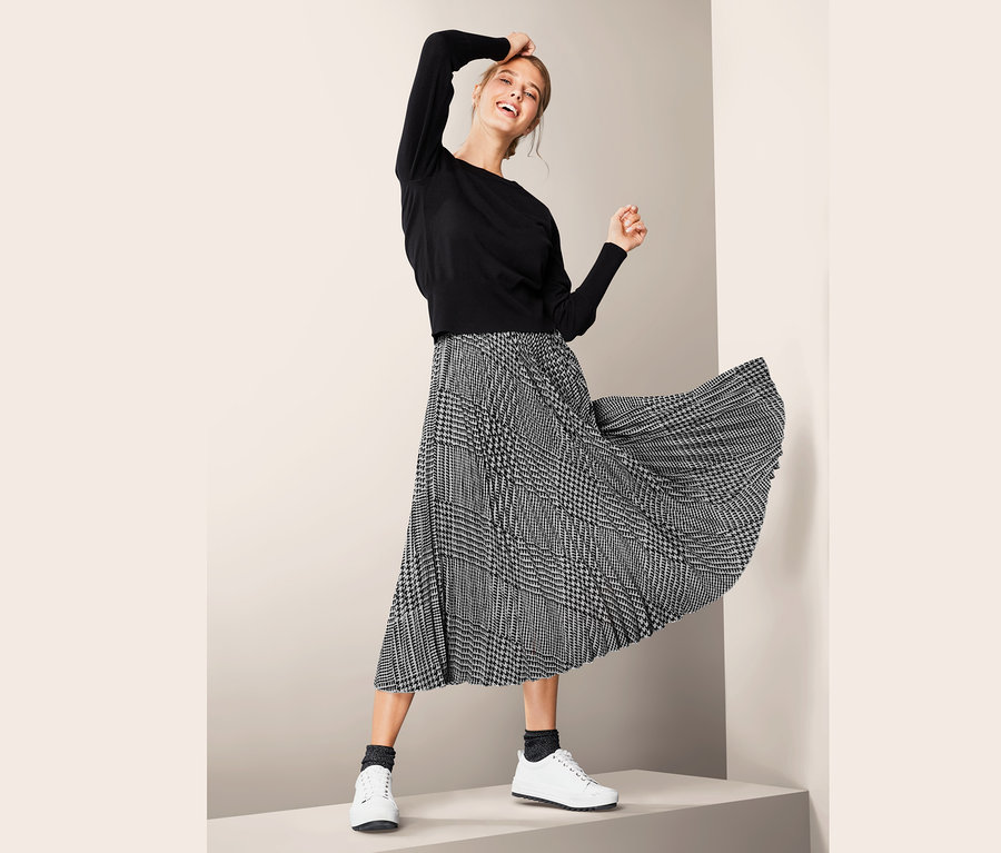 Lächelnde Frau posiert im Plisseerock.