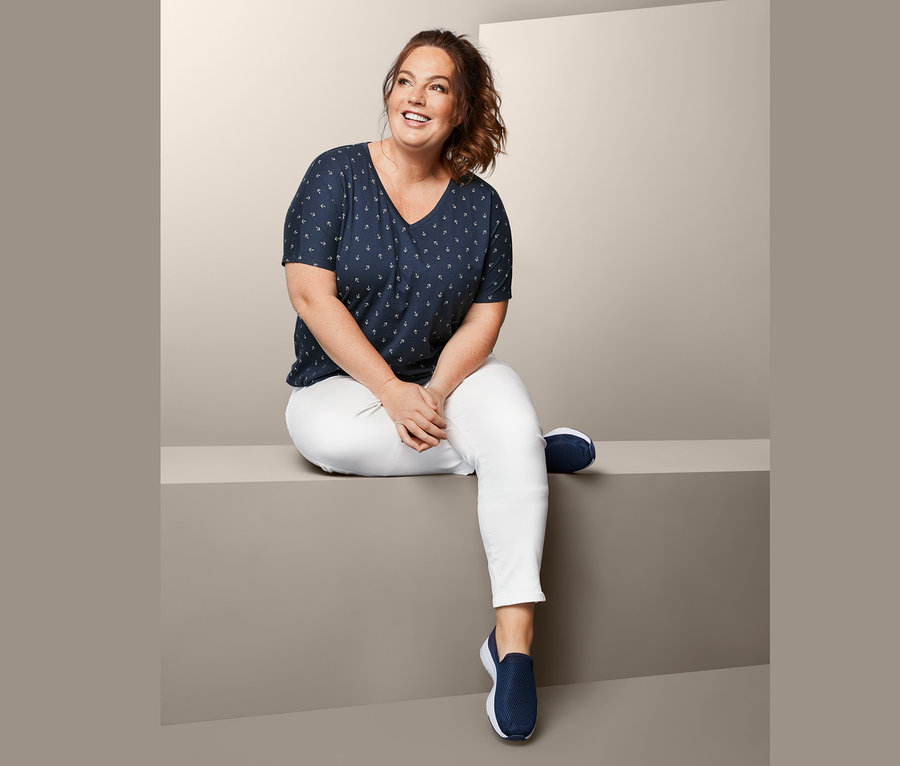 Eine Frau sitzt und trägt eine knöchellange Hose und ein Blusenshirt.