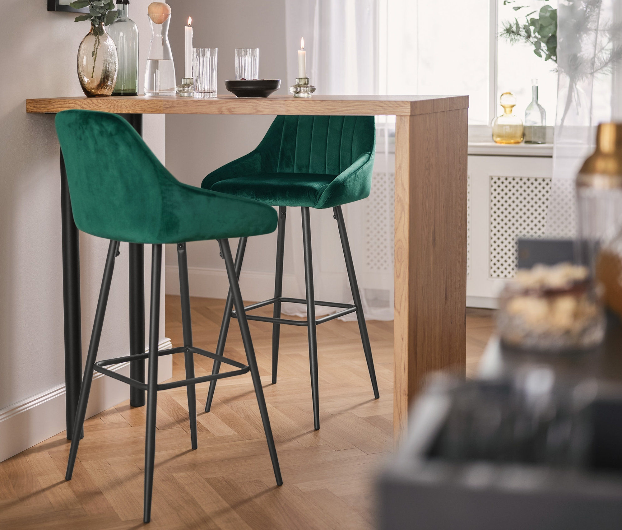 Zwei Barhocker stehen an einem Designer Bartisch »Budgie«, darüber hängt eine 4-flammige Hängeleuchte mit Textilschirm.